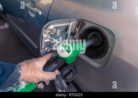 Fuel pistols at european Petrol station. Woman's hand in plastic glove putting 95 E5 fuel  green pistol to the fuel tank. Focus on the pistol. Stock Photo
