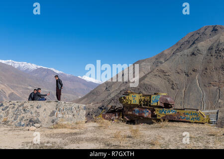 Young Men Besides Tanks Left after the Soviet-Afghan War, Panjshir Valley, Panjshir Province, Afghanistan Stock Photo