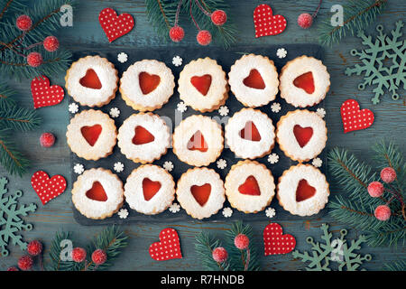 Top view of traditional Christmas Linzer cookies with red jam on rustic wooden background decorated with berries, hearts and snowflakes Stock Photo
