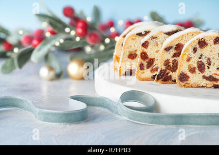Christmas stollen on white-blue festive background with berries and Xmas lights. Traditional German dessert for Christmas celebration. Stock Photo