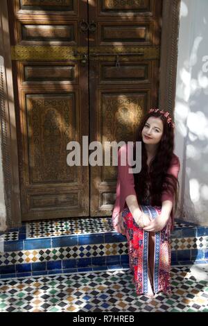 A hippie girl wearing pink clothes and hair flowers sits in a Moroccan doorway Stock Photo