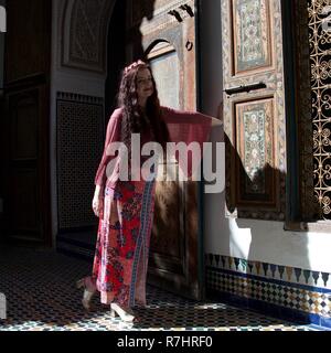 A hippie lady with wide pink sleeves poses by a door in Morocco Stock Photo