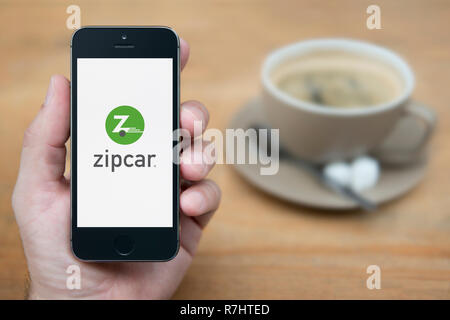 A man looks at his iPhone which displays the ZipCar logo (Editorial use only). Stock Photo