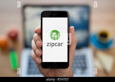 A man looks at his iPhone which displays the ZipCar logo (Editorial use only). Stock Photo