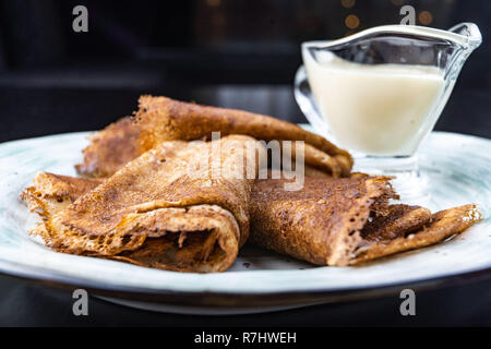 Stack of pancakes on a plate with sour cream. Traditional for the Russian pancake week. Dark background Stock Photo