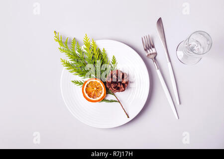 Christmas minimalistic table setting. Plate and cutlery decorated with coniferous twig and dry orange. Stock Photo