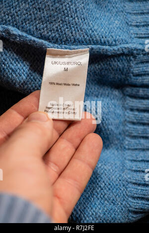 Labels for clothing composition. Instructions for washing inside on blue woolen sweater. Hand holding label inside the cloth. Stock Photo