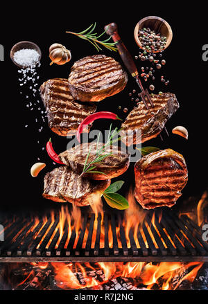 Grilled beef steaks with vegetables and spices fly over the blazing grill barbecue fire. Concept of flying food. Stock Photo