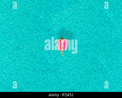 Aerial view of woman floating on inflatable donut shaped mattress, relaxing on transparent sea. Stock Photo