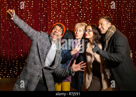 Group of friends taking funny selfie in front of light wall at Christmas market. Stock Photo