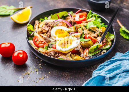 Tuna salad with pasta, olives, vegetables and poached egg in a black plate on a dark background. Stock Photo