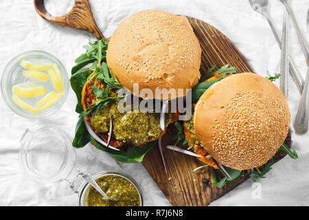 Vegetarian burger made of pumpkin cutlet, spinach, arugula and pesto sauce served on a wooden board top view. Healthy vegetarian food concept Stock Photo