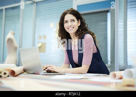 Smiling creative designer using laptop in tailoring studio Stock Photo