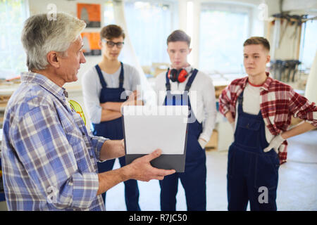Serious woodworking master explaining project to young students Stock Photo