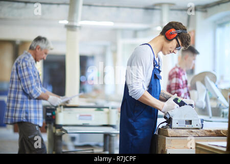 Concentrated young worker holding circular saw tight while cutti Stock Photo
