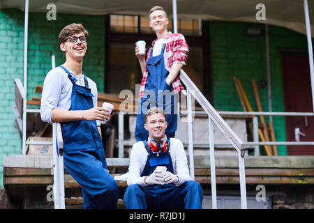 Excited industrial workers drinking coffee at break outdoors Stock Photo