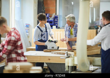 Senior carpenter teaching young worker at factory Stock Photo
