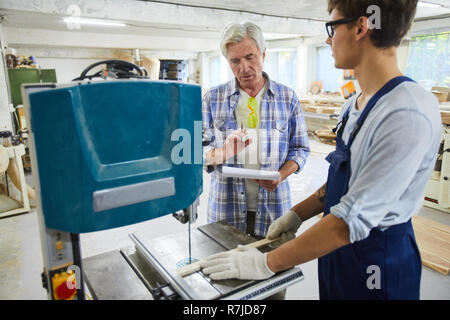 Pensive senior carpenter examining work of intern in workshop Stock Photo
