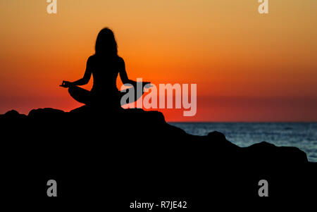 Argelès-sur-Mer (south-eastern France). Someone practising yoga on the rocks in front of the Racou Beach at sunrise. Beautiful young woman with long b Stock Photo