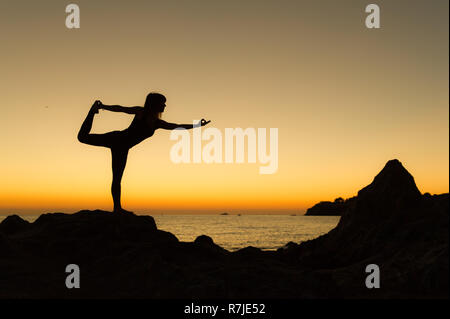 Argelès-sur-Mer (south-eastern France). Someone practising yoga on the rocks in front of the Racou Beach at sunrise. Beautiful young woman with long b Stock Photo