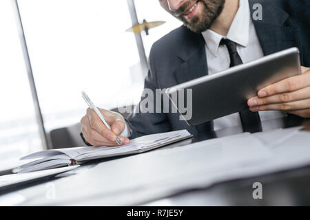 Businessperson on business lunch at restaurant sitting taking notes in organizer holding digital tablet joyful Stock Photo