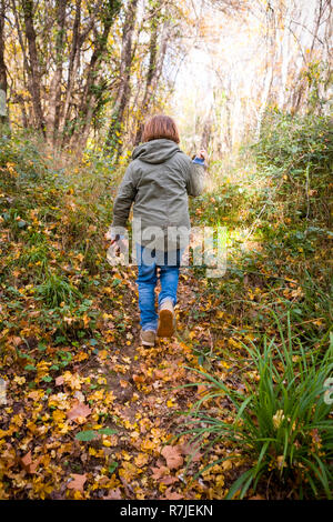 rear view of 11 year old boy with khaki hooded coat and jeans walking down a leafy path in a wood in Autumn, france Stock Photo