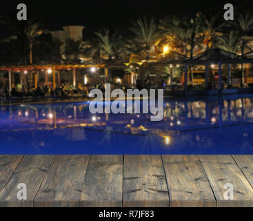 Empty wooden plank with view to evening tropic party. Table top with at evening resort. Vintage boards with people relaxing at modern night resort Stock Photo