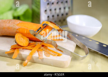 Fresh carrot grated on a metal kitchen grate. Vegetables prepared for salad with a meal on the kitchen table. Light background. Stock Photo