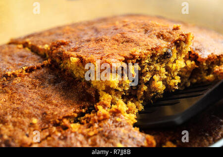 A crumbly square slice of freshly baked carrot cake being lifted from baking dish for serving. Close up just above eye level. Stock Photo