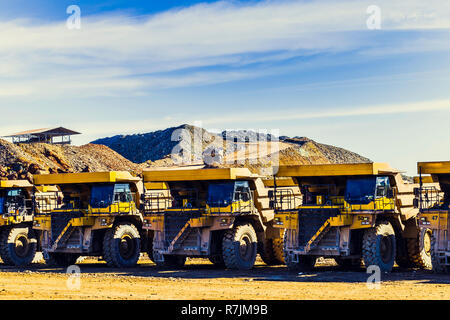 Big yellow dumpers put in a row in the mine with tipper laden with ore along the way with the blue sky with clouds in the background Stock Photo