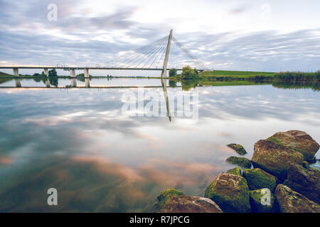 Sunset in the Dutch river delta with the reflection of a bridge mirrored in the IJssel stream, Near Kampen, Holland Stock Photo