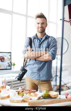 Waist up portrait of smiling photographer looking at camera while posing in photo studio Stock Photo