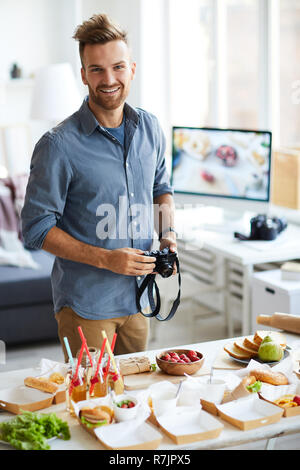 Waist up portrait of smiling photographer looking at camera while taking pictures of party table with food Stock Photo