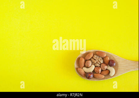 Assorted Nuts In A Wooden Spoon On Yellow Background. Healthy Organic Snack, Breakfast, Food Ingredients. Flat Lay Top-Down Composition. Stock Photo