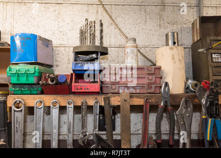 Parts screws and other small items on a shelf with a range of spanners (wrenches) hanging on screws from the same shelf in a workshop Stock Photo