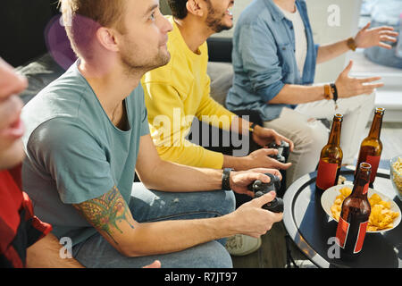 Concentrated young man sitting on sofa with joystick and playing with his friends in video games at home Stock Photo