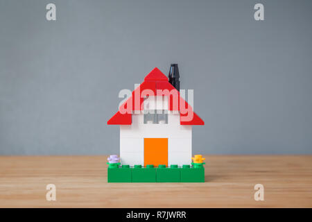 Small and simple house made of toy building bricks, on a wooden surface, gray background. Viewed from the front. Copy space. Stock Photo