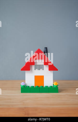 Small and simple house made of toy building bricks, on a wooden surface, gray background. Viewed from the front. Copy space. Stock Photo