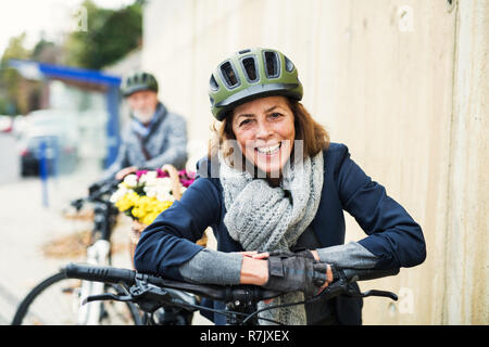 Active senior couple with electrobikes standing outdoors on a pathway in town. Stock Photo