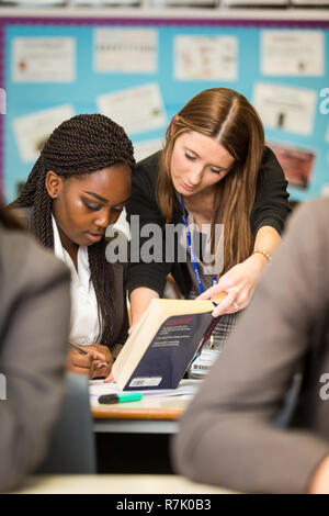 White teacher helping a black ethnic minority schoolgirl in a UK british school Stock Photo