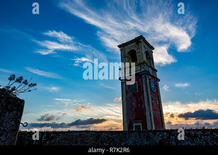Medieval clock tower in the fort of Corfu, Greece at sunset with the Sun low behind the building, scenery colorful cloudy spring sky Stock Photo