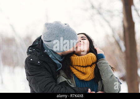 Happy woman and man, kissing, and huging, spending time together enjowing eachother, snow, life, winter. Portrait wonderful young couple wearing styli Stock Photo