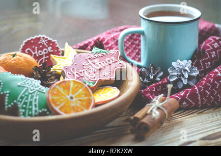 Christmas card: A cup of hot tea stands on a wooden table next to a wooden plate on which are gingerbread cookies made from orange slices against the  Stock Photo