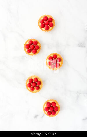 Homemade tartlets filled with fresh raspberries and lemon cream on white marble background. Top view. Stock Photo