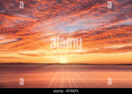 Dramatic, fiery yellow, golden, red and magenta sunrise sky with sun and sun rays over the sea. Stock Photo