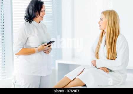 Woman with beautician gets appointment for next visit, uses smartphone in salon Stock Photo