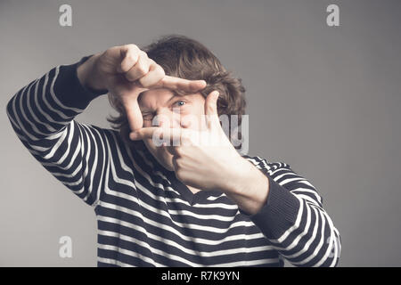 Young handsome man focusing with fingers, framing with hands isolated on grey background. Close up portrait. Stock Photo