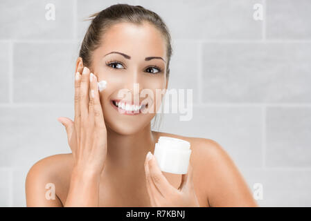 Cute girl preparing to start her day. She is applying moisturizer cream
