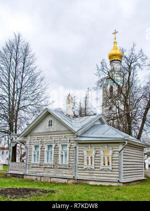 Old wooden house on a green meadow with carved windows. Church in the background. Russian old house. izba Stock Photo