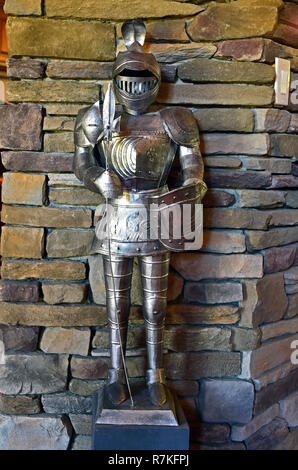 A replica of a suit of medieval armour on display in front of a stone wall Stock Photo